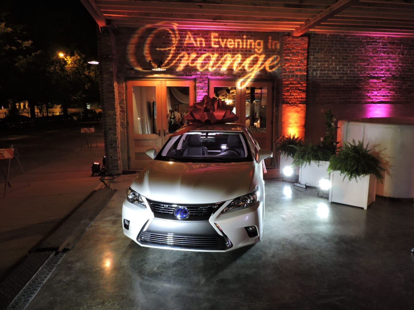 A sleek silver Lexus car is showcased indoors with warm orange lighting.