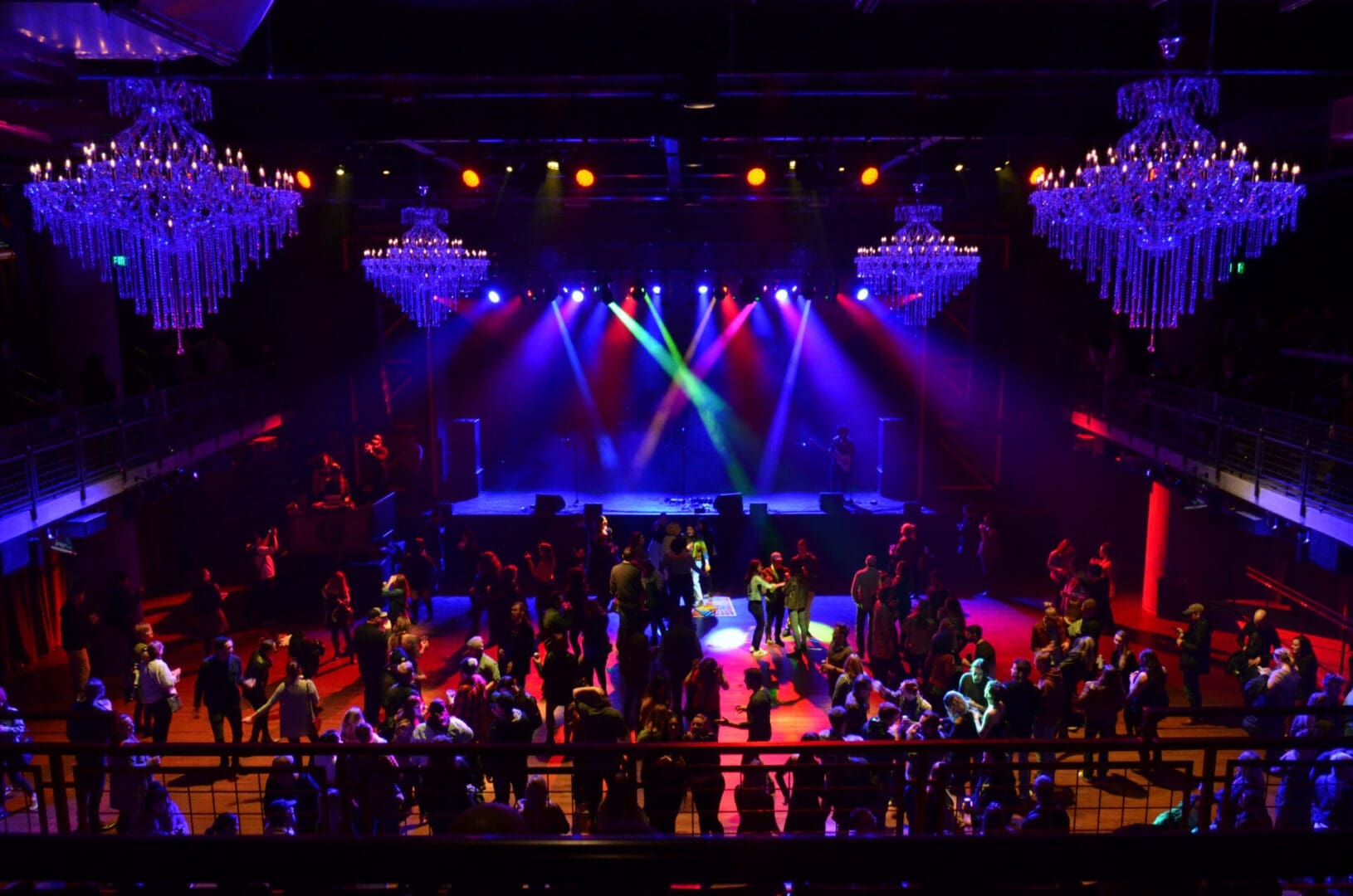 Colorful stage lights illuminate a lively concert crowd in a grand venue.