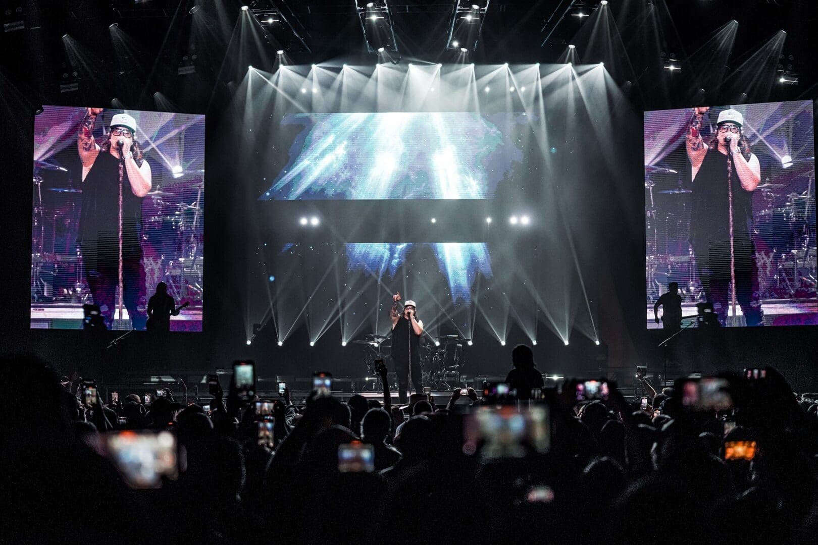 A performer on stage with dramatic lighting and a large crowd.