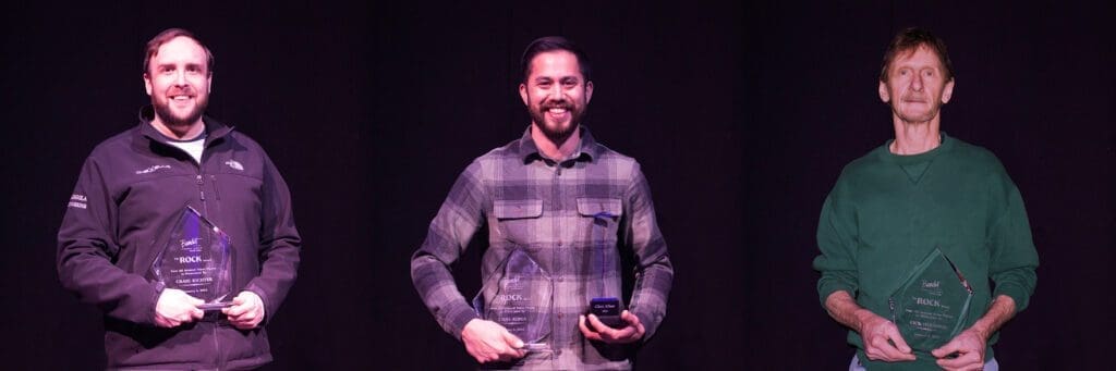 Smiling man in a plaid shirt holding an object on stage.