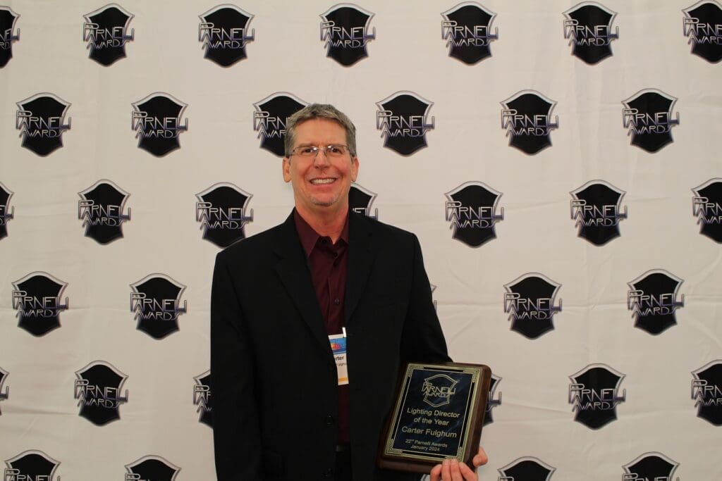 Man in suit holding an award plaque, smiling at the camera.