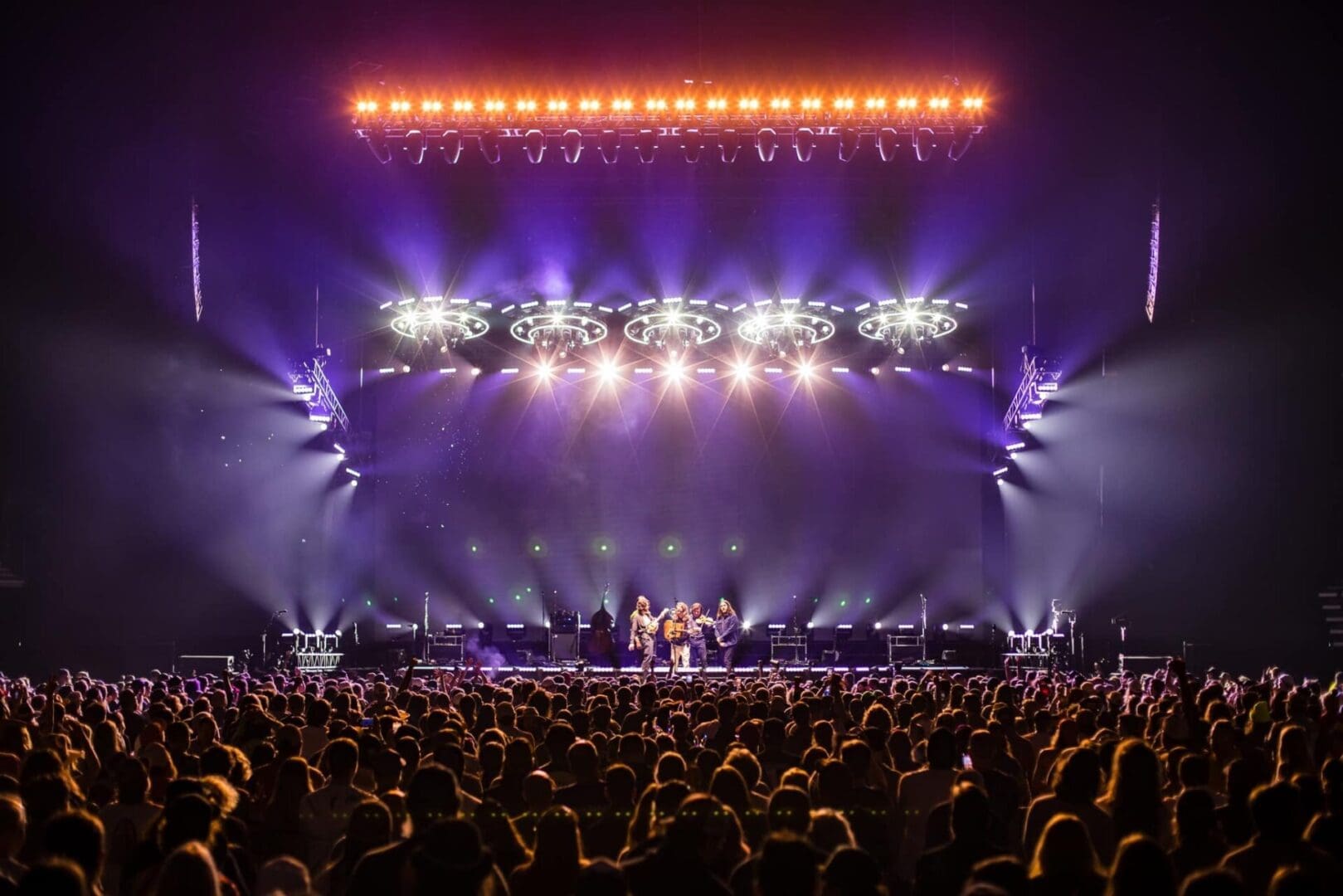 A vibrant concert scene with bright stage lights and a large enthusiastic crowd.