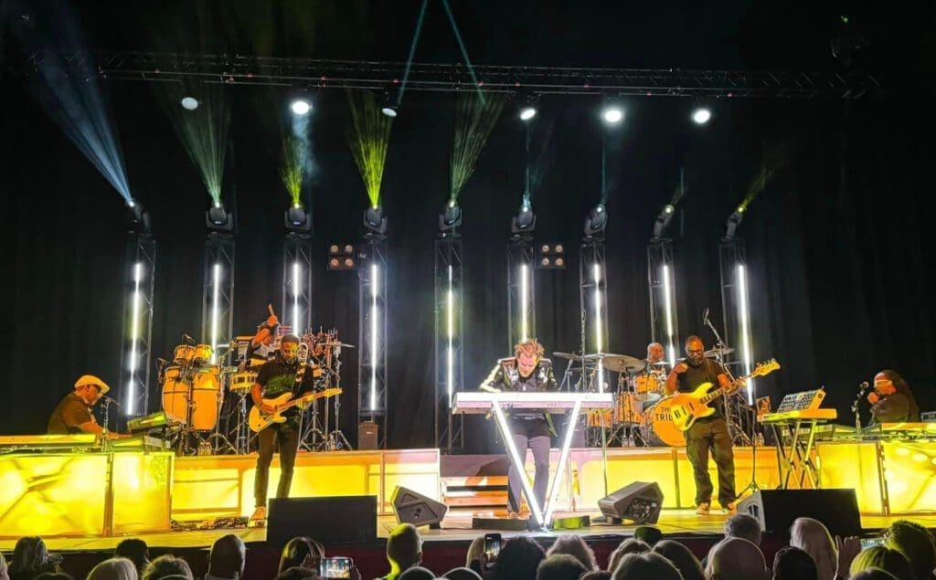 A live band performs on stage with colorful lighting and enthusiastic audience.