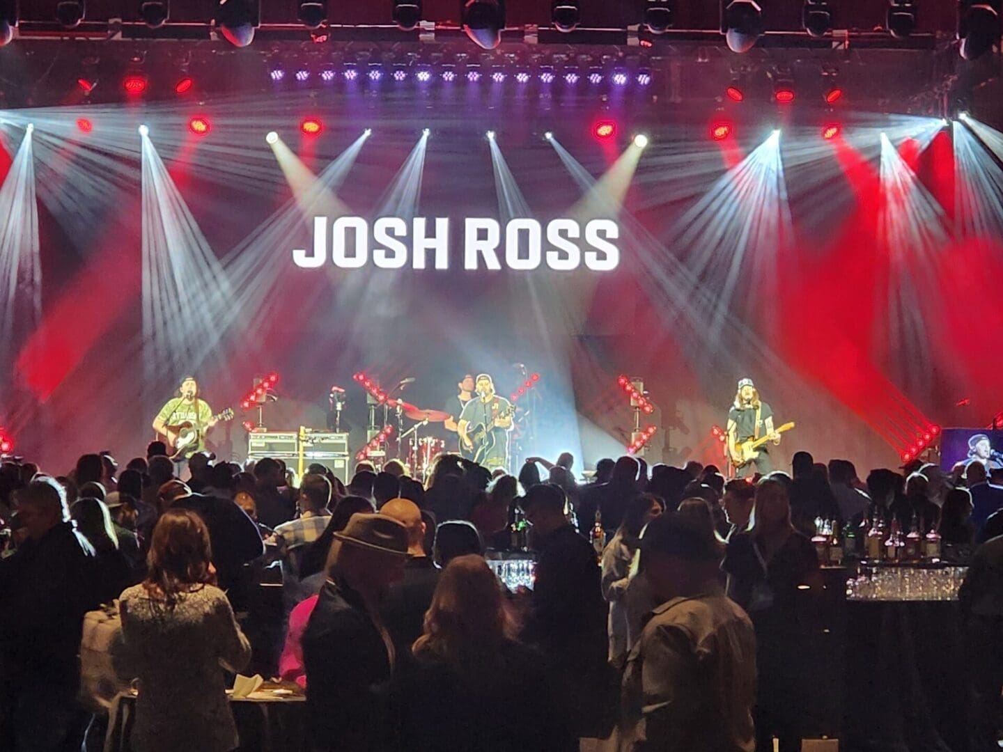 A live band performs on stage with bright spotlights and a crowd watching.