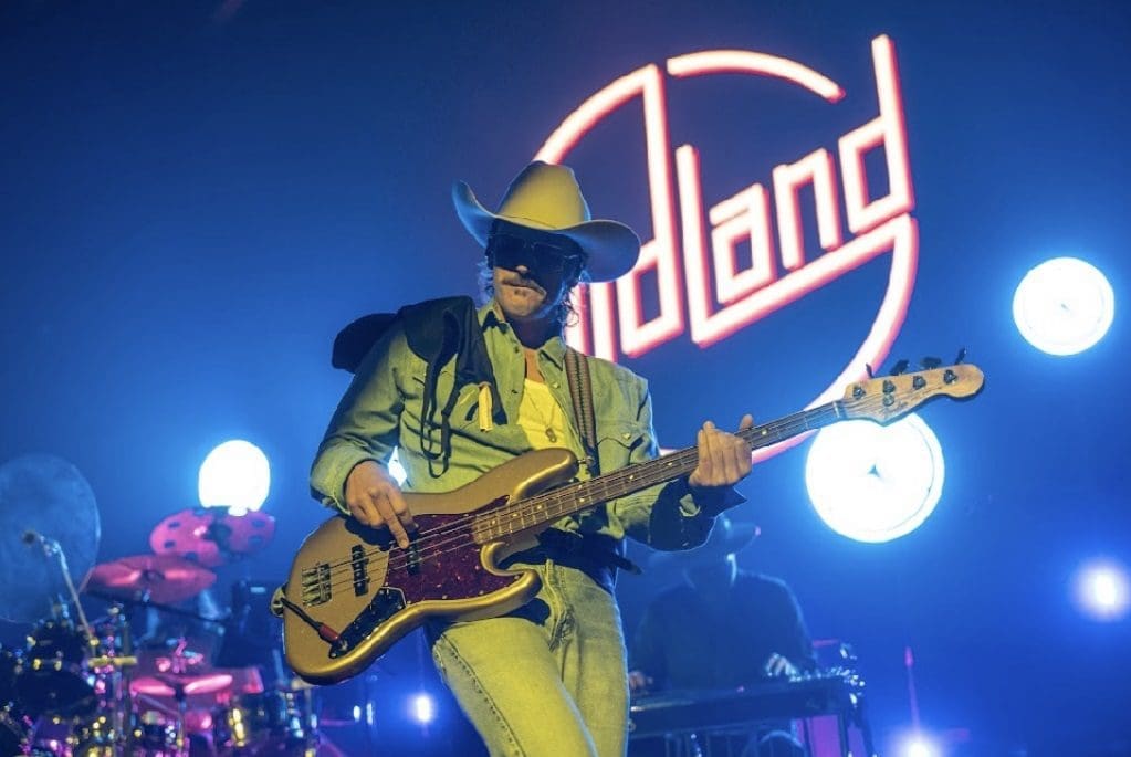 Musician playing electric guitar on stage with vibrant blue lighting and "Holland" sign.