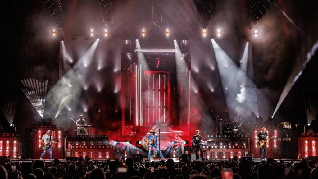 A rock band performs on a brightly lit stage with red and white lights.