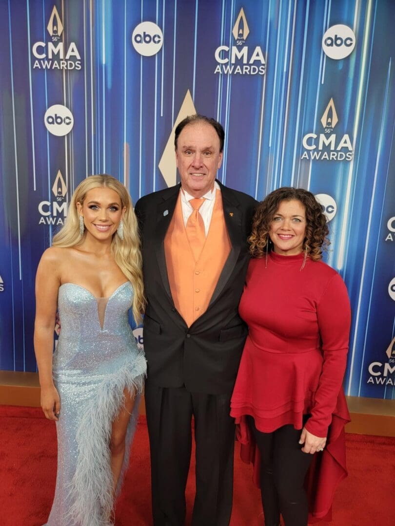 Three people posing on the red carpet at the CMA Awards.