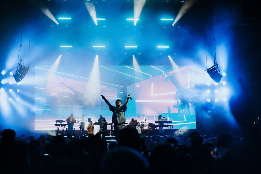 Silhouetted singer performs energetically on a brightly lit stage.