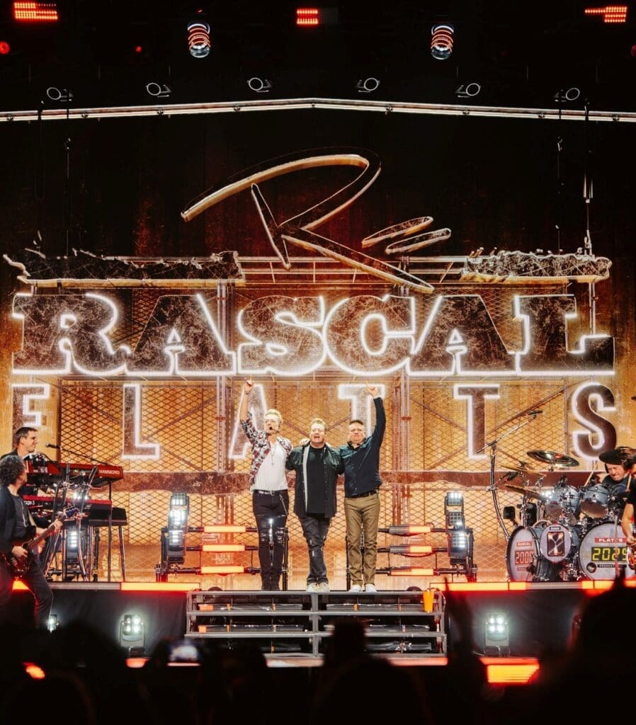 Performers on stage at Rascal Flatts concert with vibrant lighting.