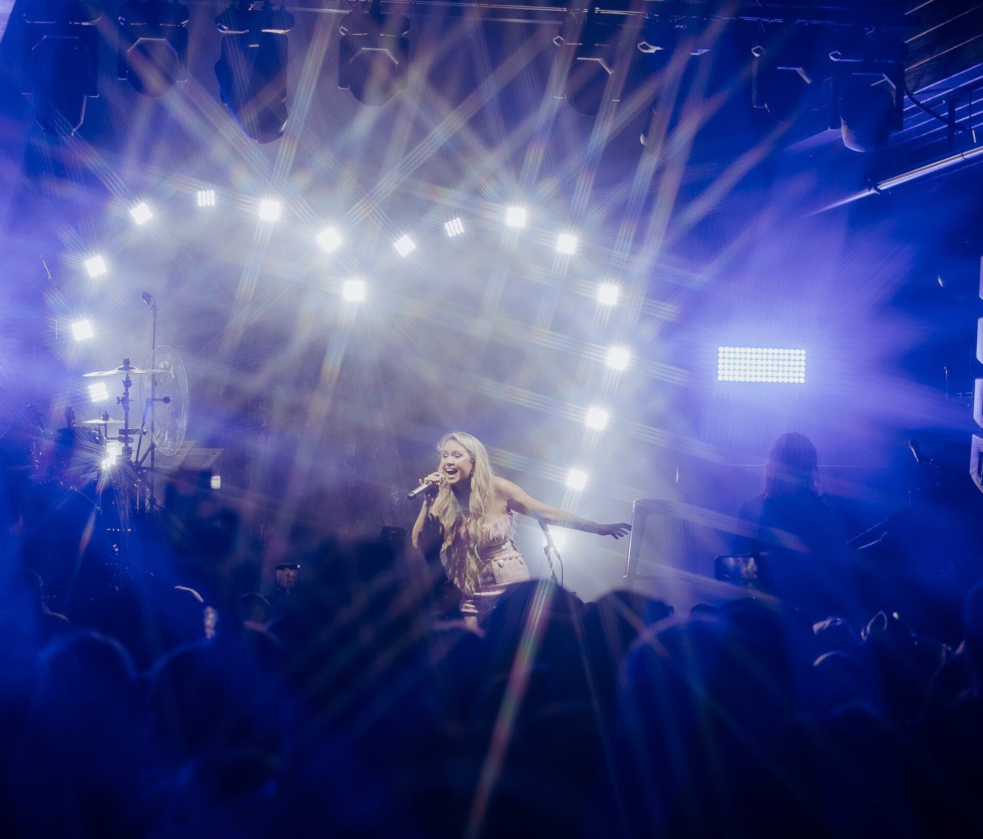 Singer performing on stage under bright lights with a lively crowd.