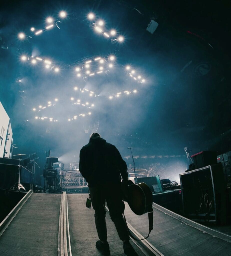 A silhouetted figure walks toward a brightly lit stage in a large arena.