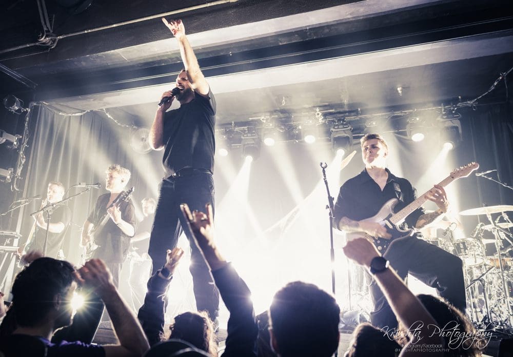 Energetic live band performing on stage with crowd cheering.