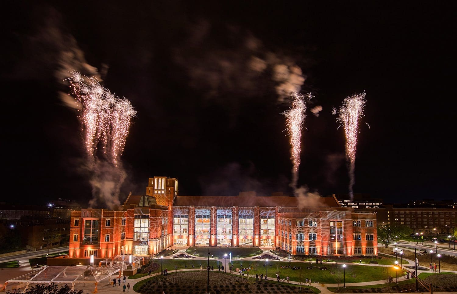 Fireworks light up the night sky above a grand building with a large lawn.