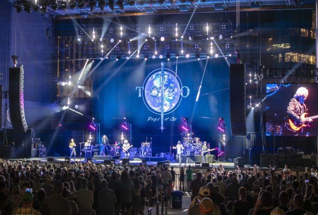 A band performing on a brightly lit stage with a large crowd.