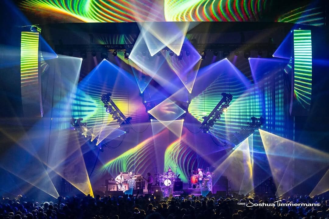 A vibrant live concert with colorful geometric light projections.