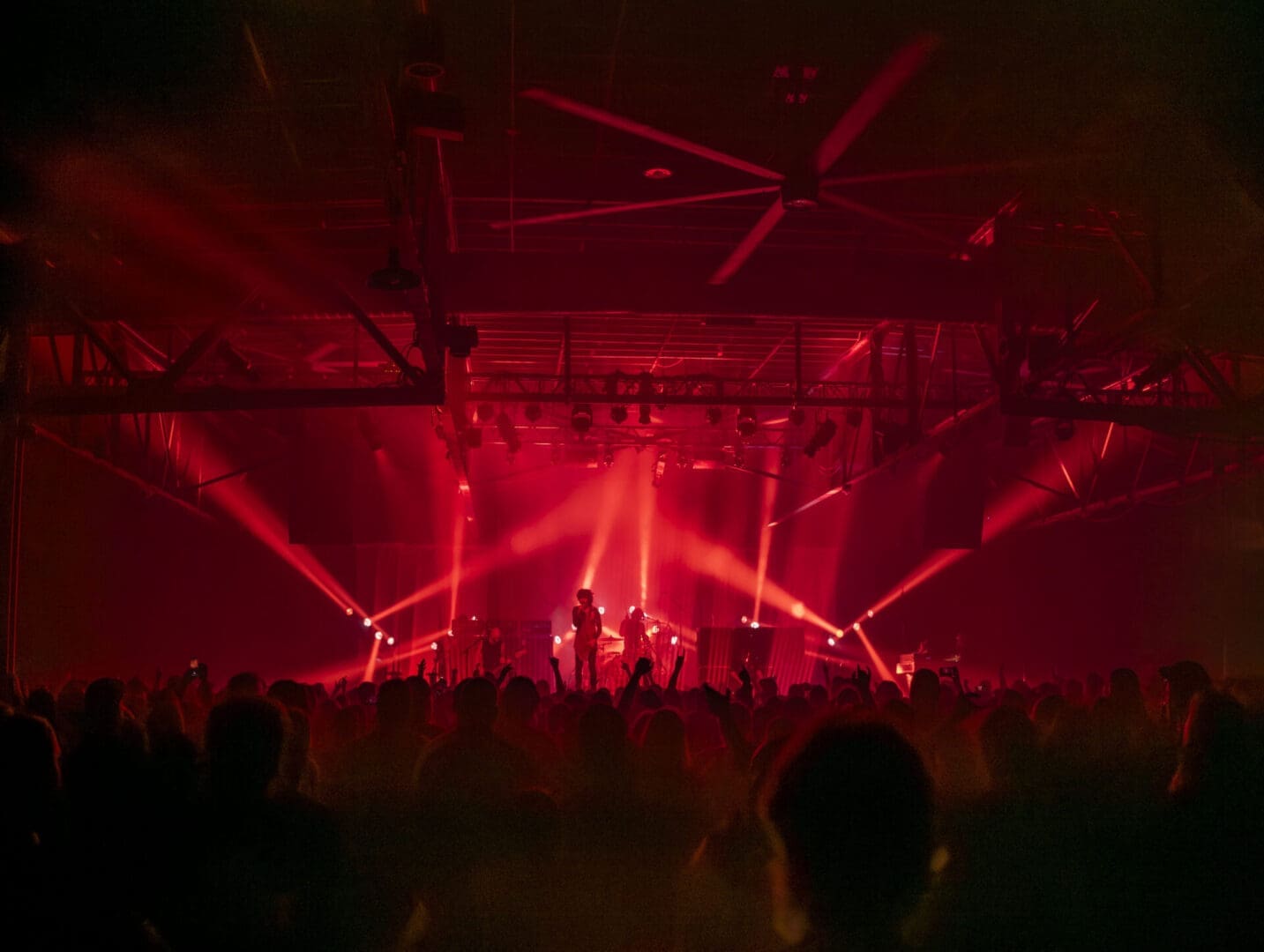 A vibrant concert with red stage lights and a large crowd.