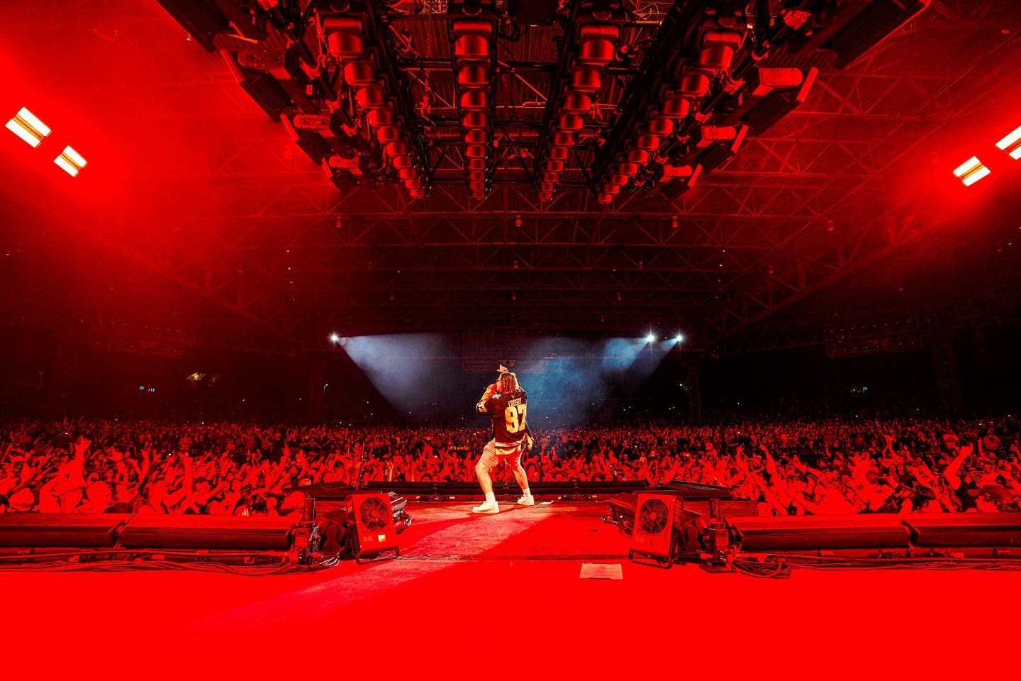 Performer on stage with vibrant red lighting and a large audience.