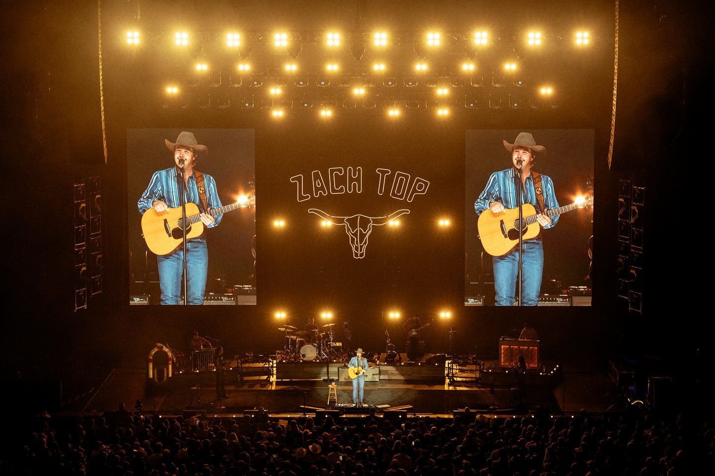 Country singer performing live on stage with guitar under bright lights.
