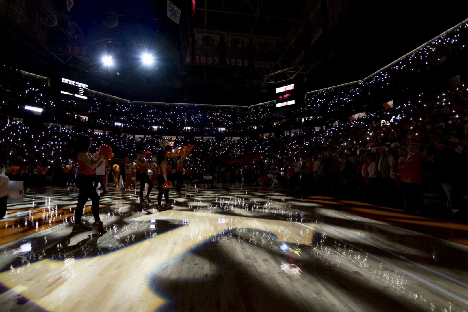 Wrestlers gather inside an arena under dramatic lighting before a match.