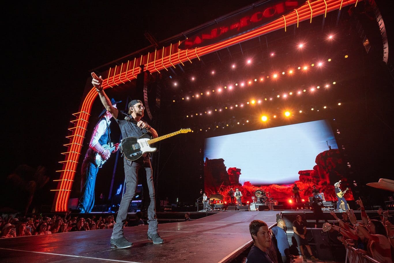 Electric guitarist performing on stage under bright lights.