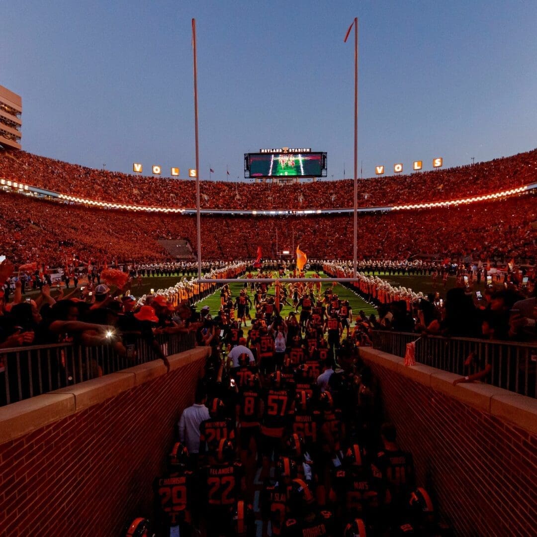 Crowded stadium during a football game with fans entering the field area.