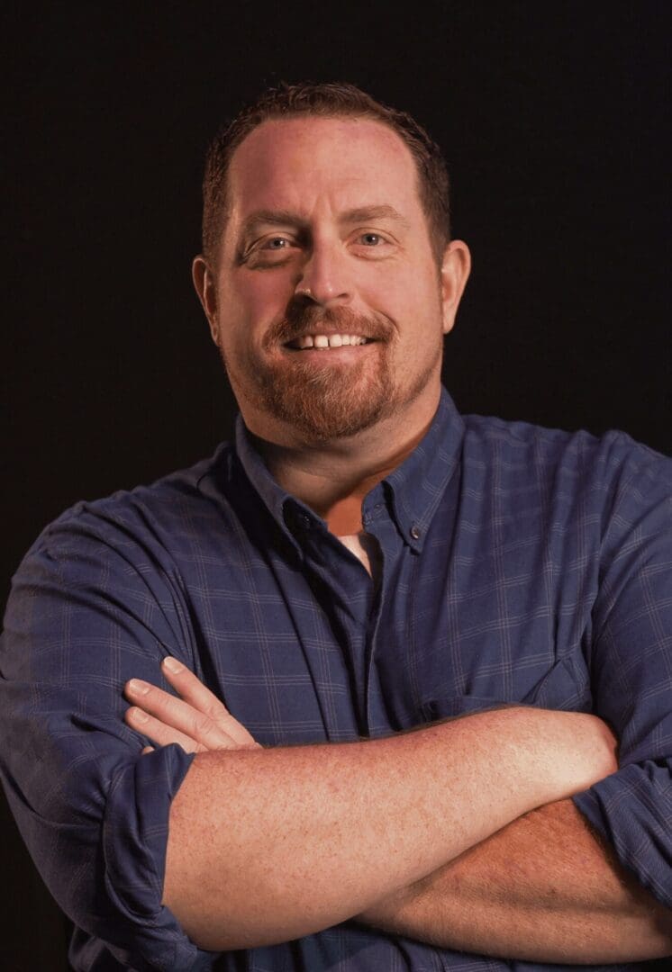 Smiling man with crossed arms wearing a blue shirt.
