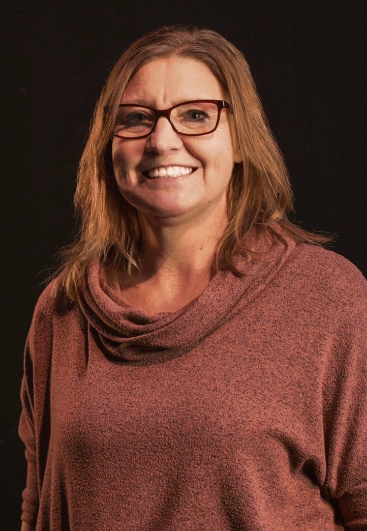 Smiling woman wearing glasses and a maroon sweater against a dark background.