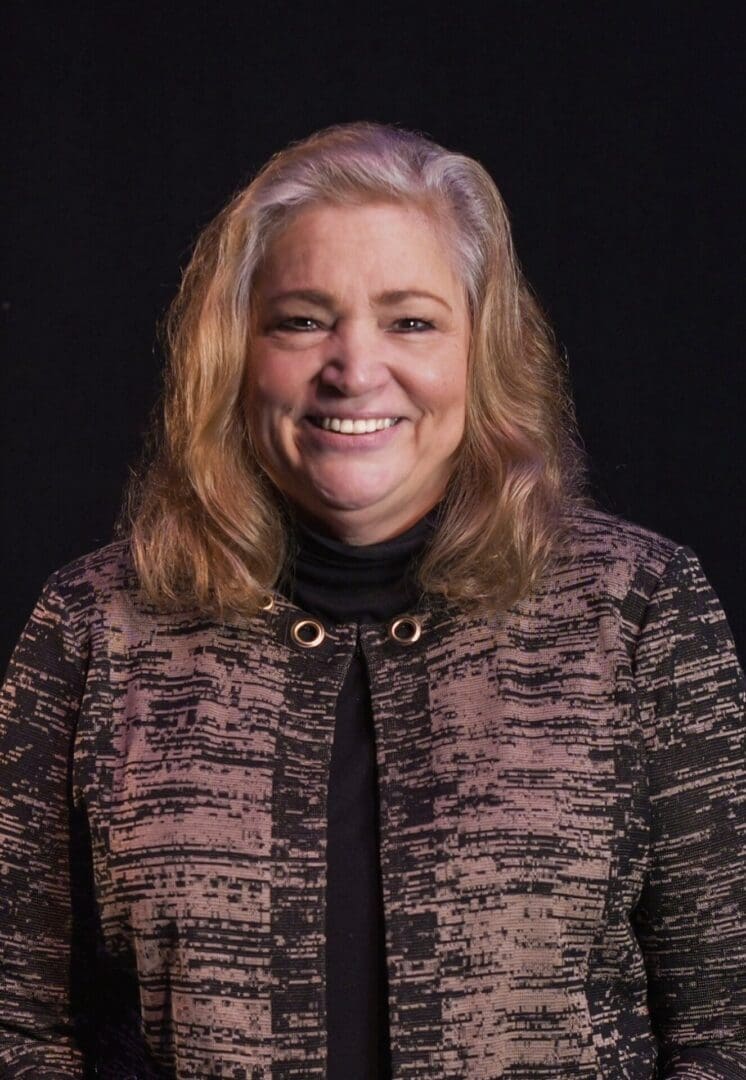 Smiling woman with light brown hair wearing a patterned jacket.