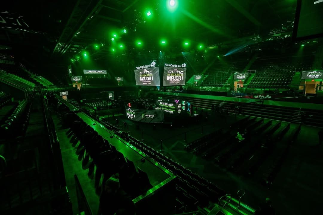 A dimly lit arena with green lights and large screens above the stage.
