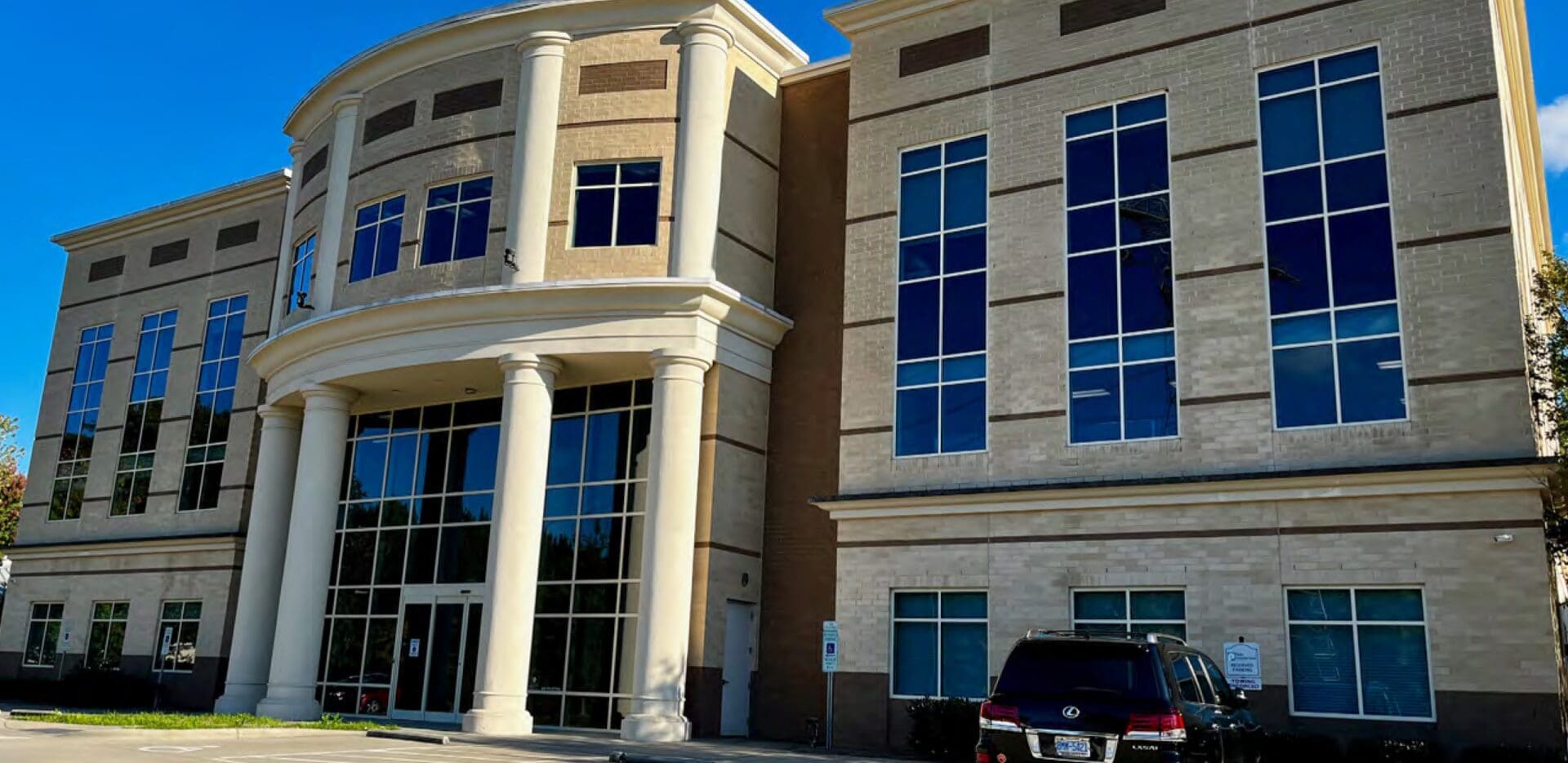 Modern beige brick building with large windows and columns at entrance.