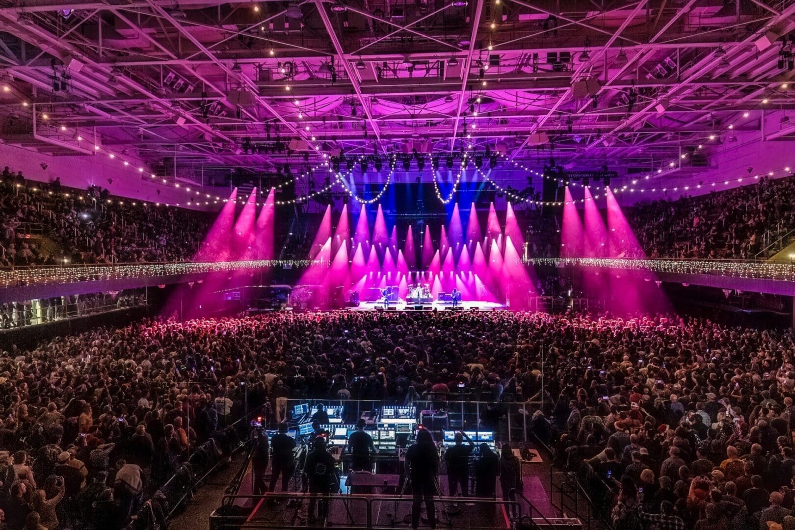 A vibrant concert with bright pink and purple stage lights and a large audience.