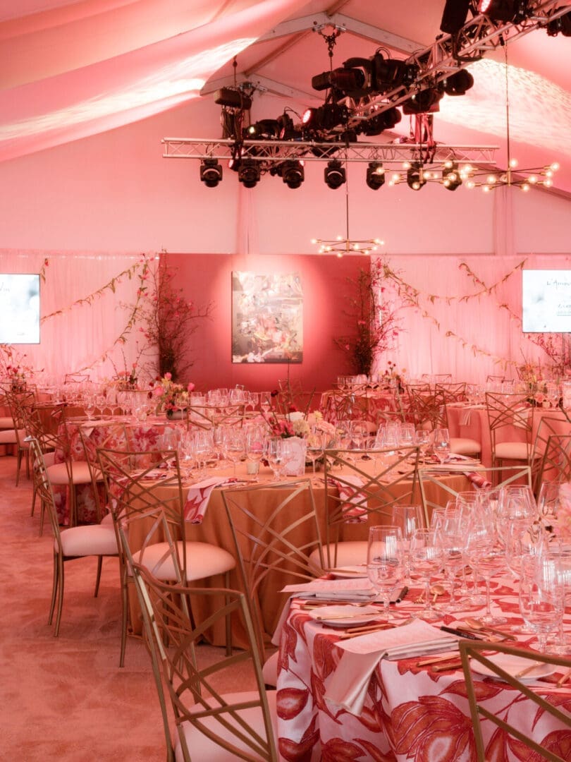 Elegant wedding reception setup with round tables and soft pink lighting.