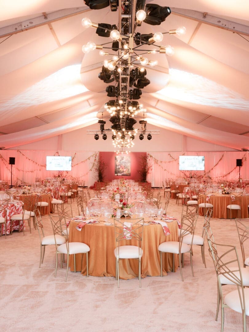Elegant wedding reception setup with round tables and soft pink lighting.