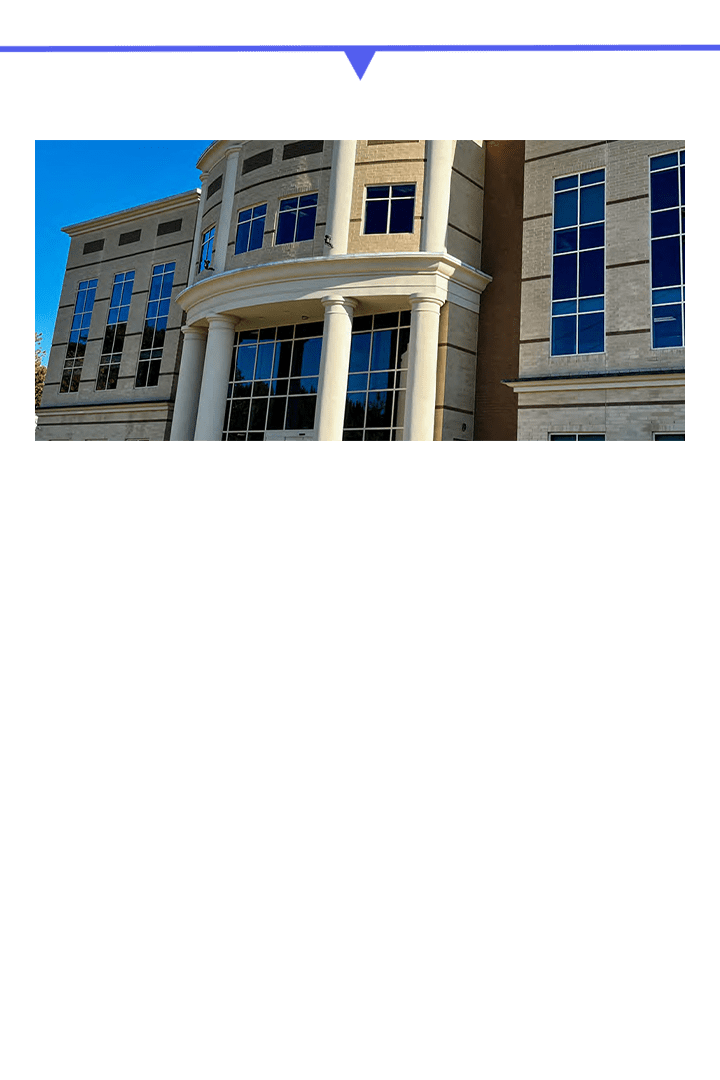 Modern stone building with large columns and windows under a clear blue sky.