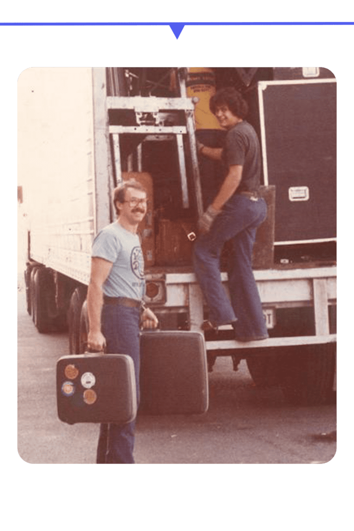 Two men carrying large dice near a truck.