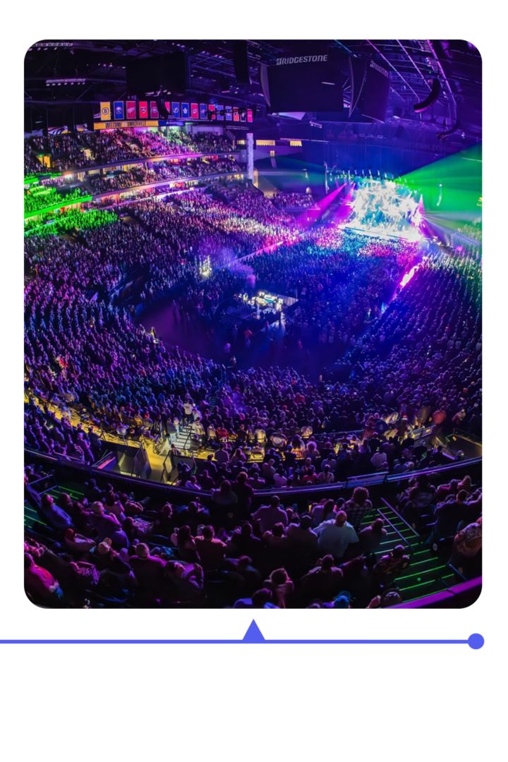 A packed arena lit with colorful lights during a concert.