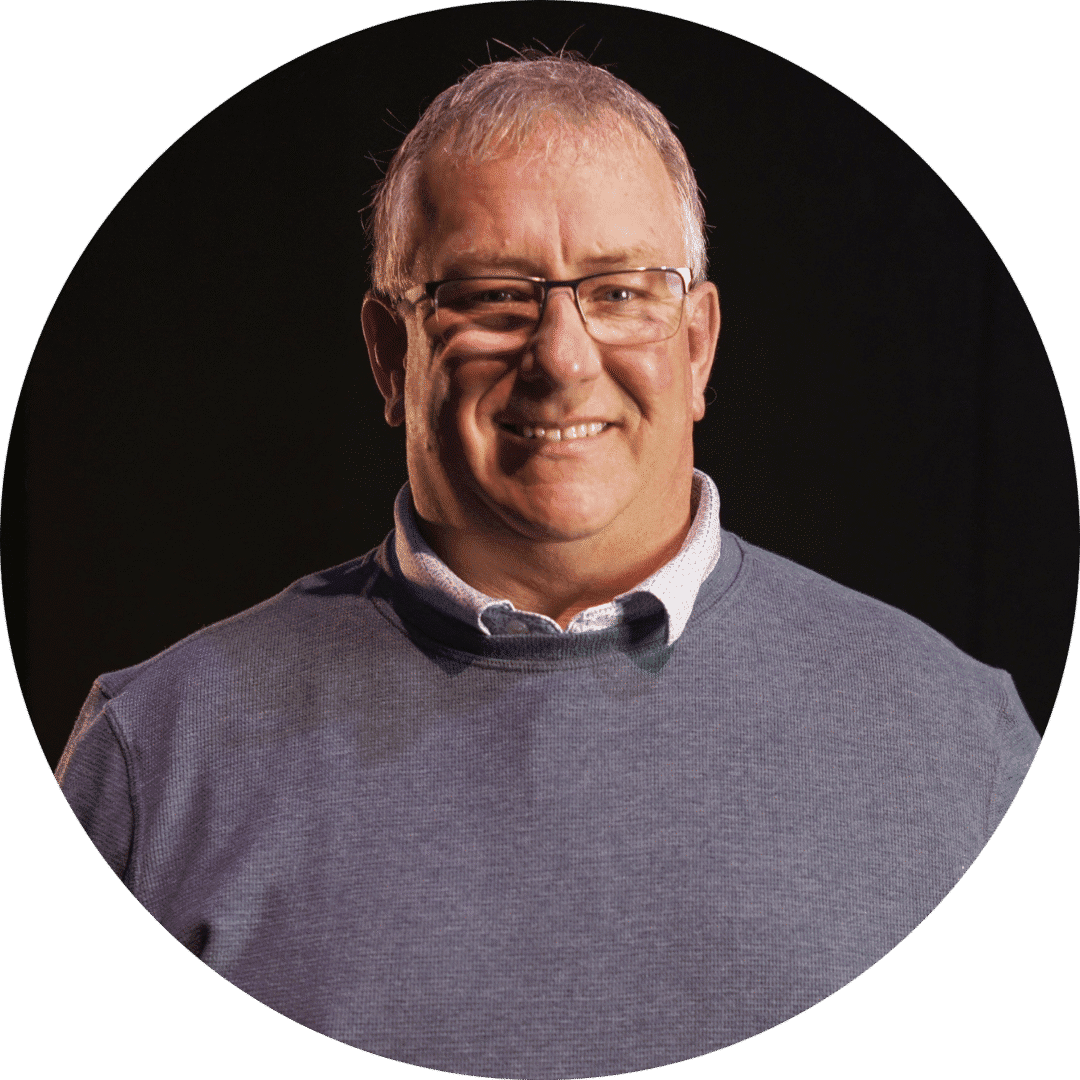 Smiling middle-aged man wearing glasses and a grey sweater.