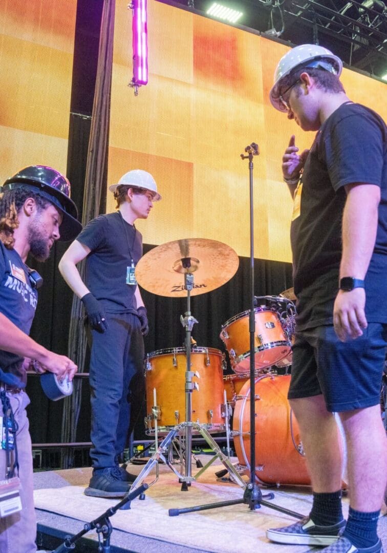 People setting up drums on a stage with bright lights.