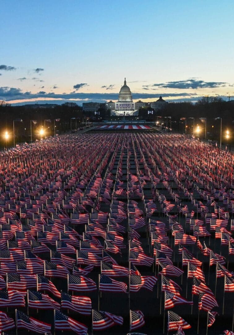 A large crowd holding American flags at dusk in front of the Capitol.