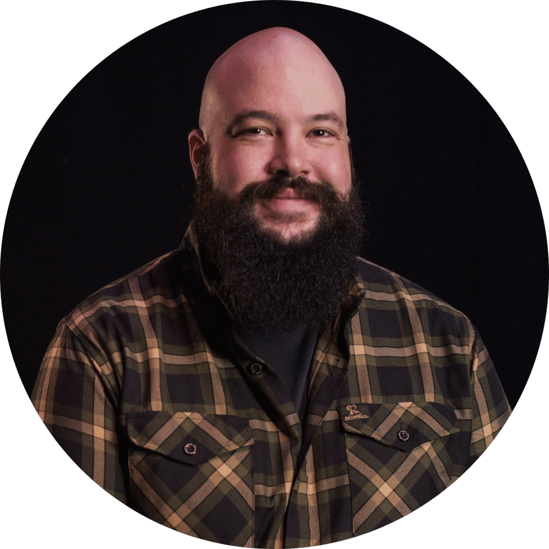 Bearded man in a plaid shirt smiling against a black background.