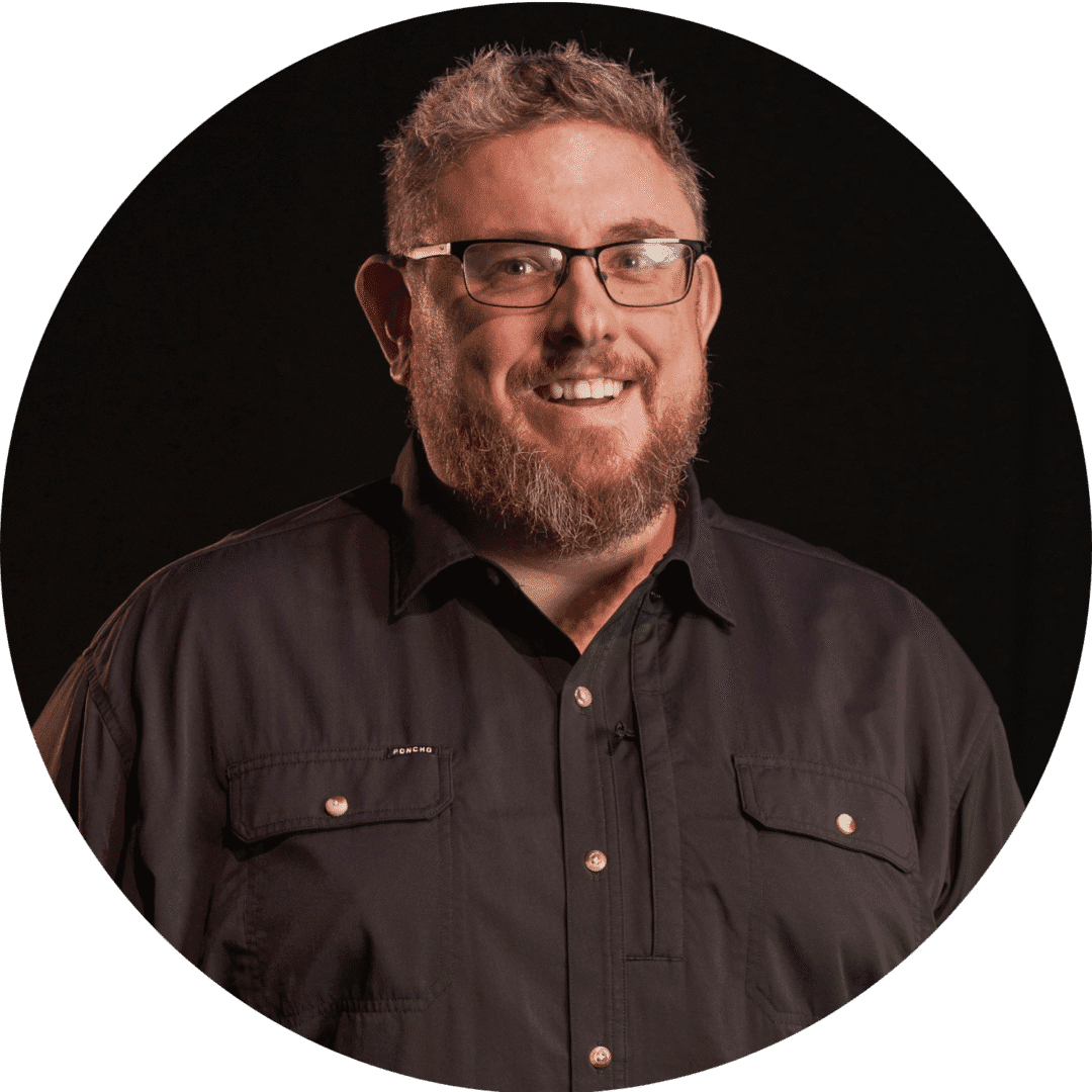 Smiling man with glasses and beard wearing a dark shirt.