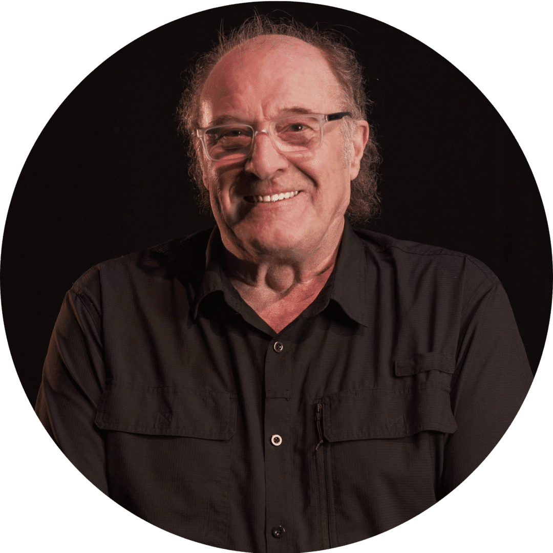 Smiling elderly man with glasses in a black shirt against a dark background.