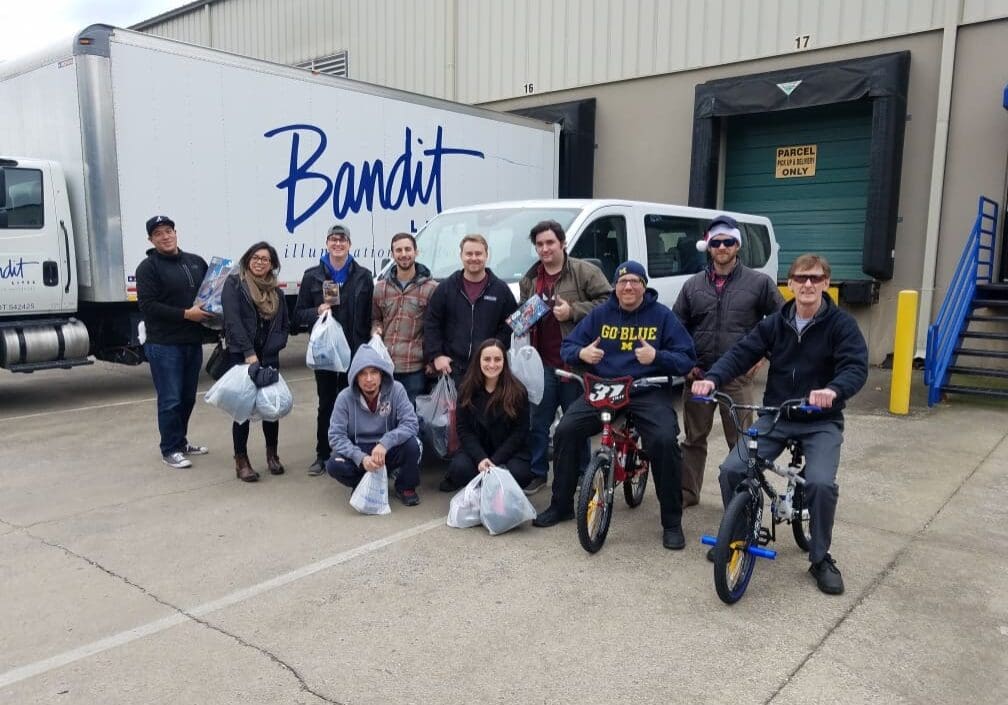 Group photo of cheerful people outside a Bandit-branded vehicle.