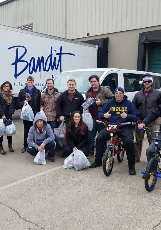 Group photo of cheerful people outside a Bandit-branded vehicle.