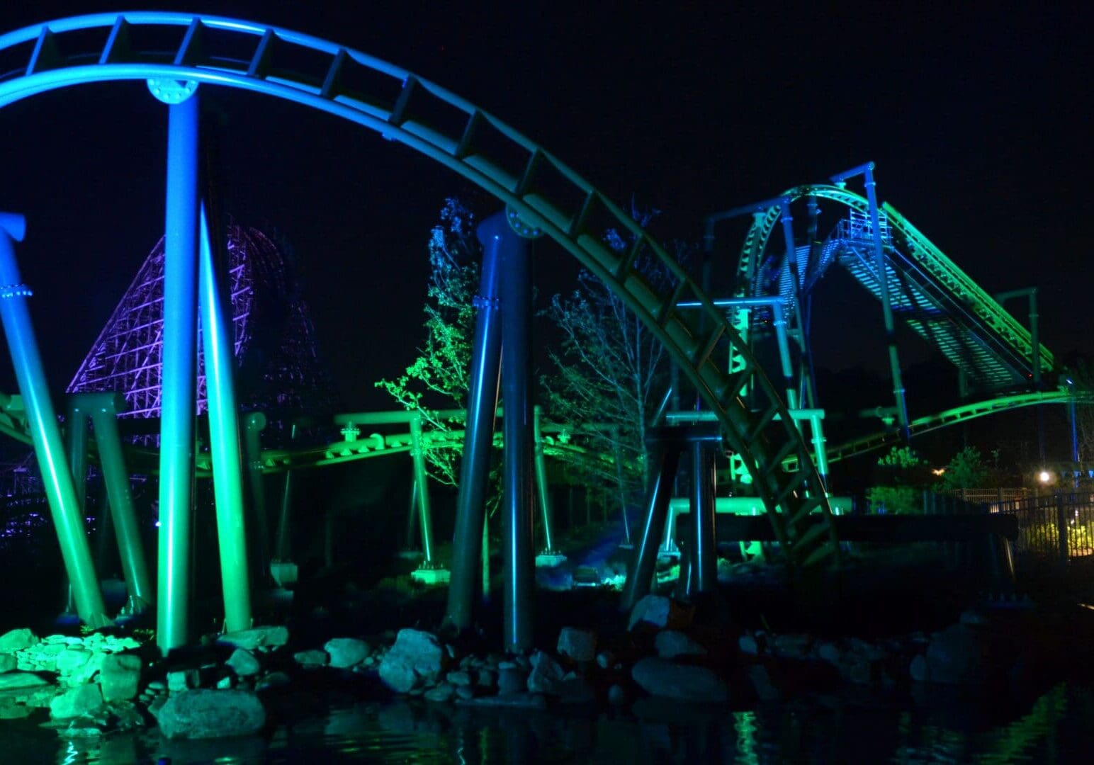 Roller coaster illuminated with green and blue lights at night.