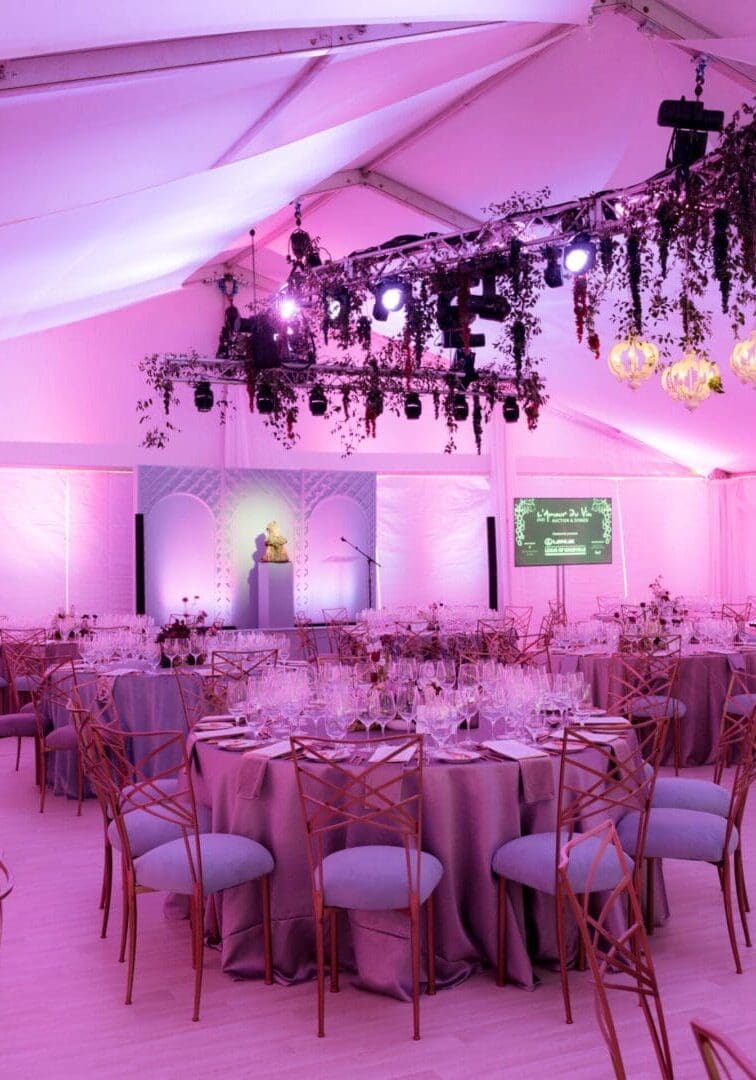 Elegant wedding reception setup with soft pink lighting and decorated tables.