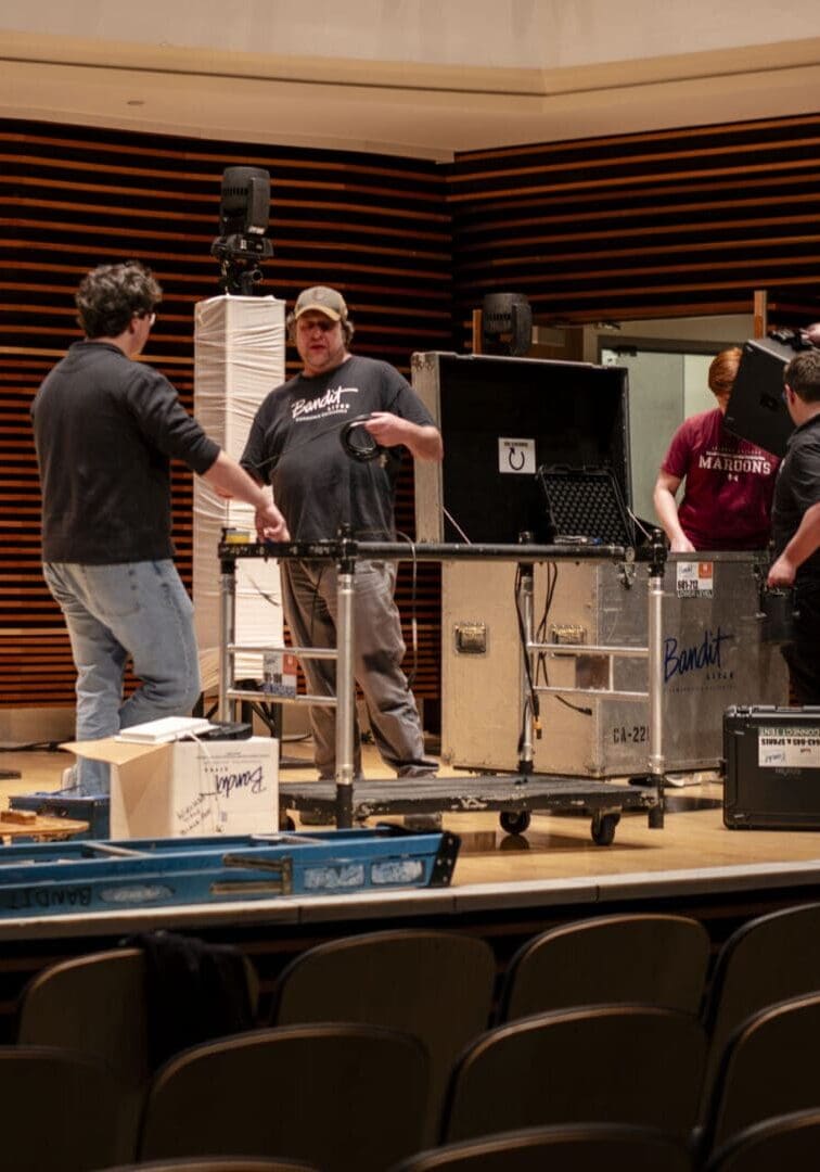 Three men setting up audio equipment in an auditorium.