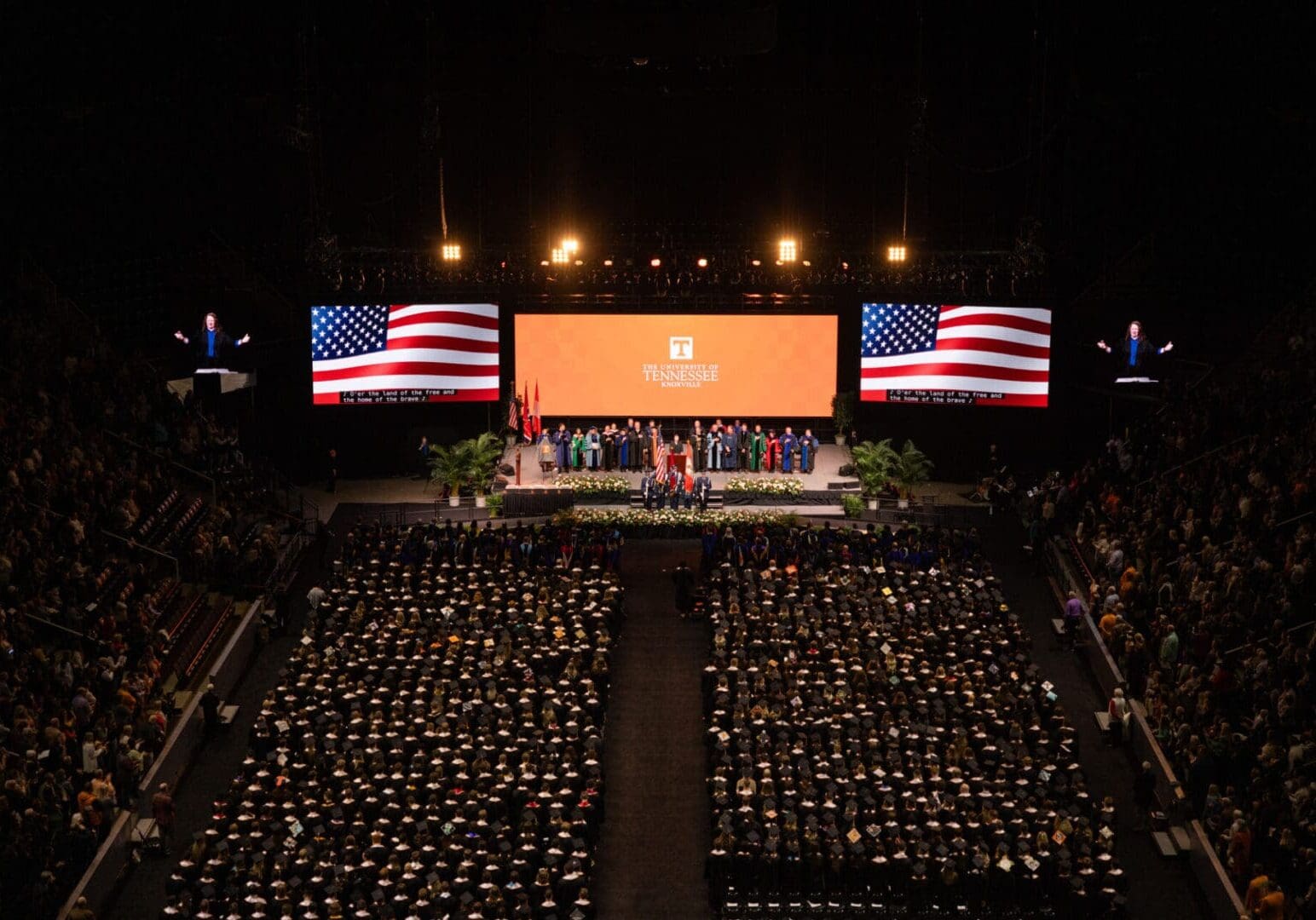 Graduation ceremony with American flags and a large crowd of graduates.
