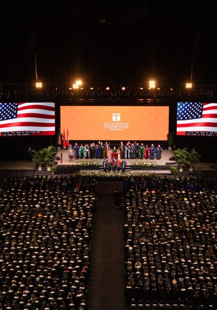 Graduation ceremony with American flags and a large crowd of graduates.