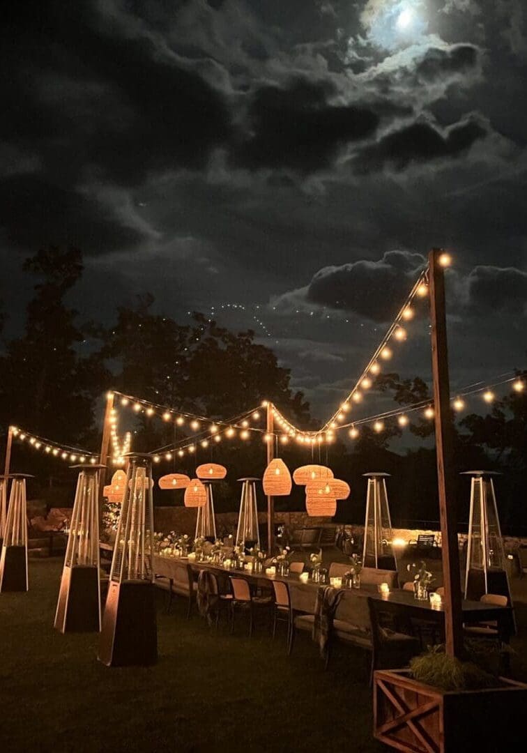 Outdoor dining setup under a moonlit sky with string lights.